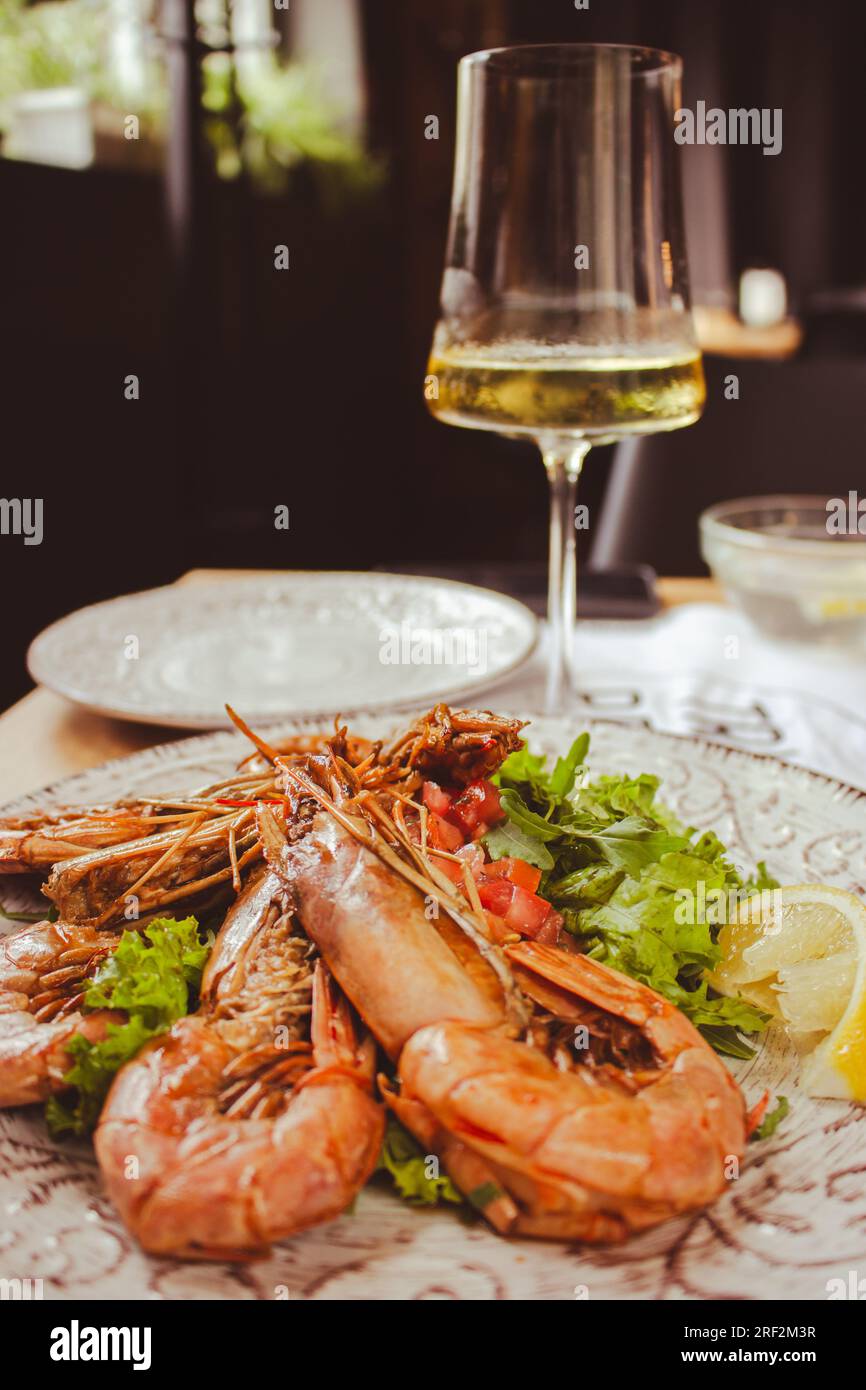 Langoustine with lemon and wine. Seafood close up. Fish dish with glass of wine. Fish restaurant menu. Grilled scampi with salad. Stock Photo