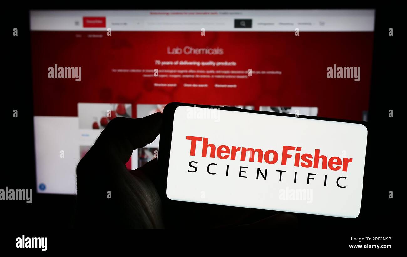 Person holding mobile phone with logo of American company Thermo Fisher Scientific Inc. on screen in front of web page. Focus on phone display. Stock Photo