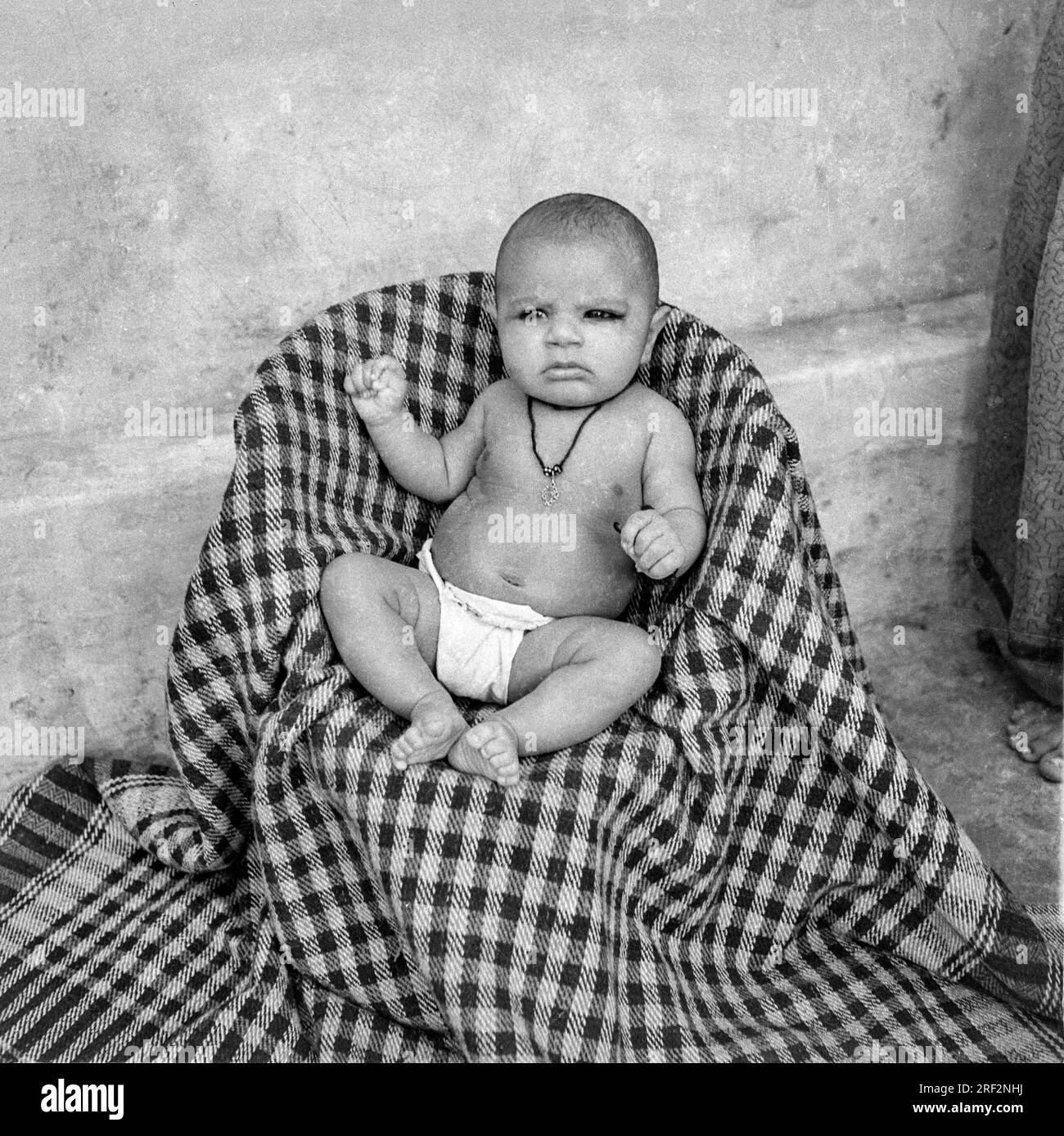 old vintage 1900s black and white studio portrait of Indian baby boy child wearing nappy diaper sitting stool India 1940s Stock Photo