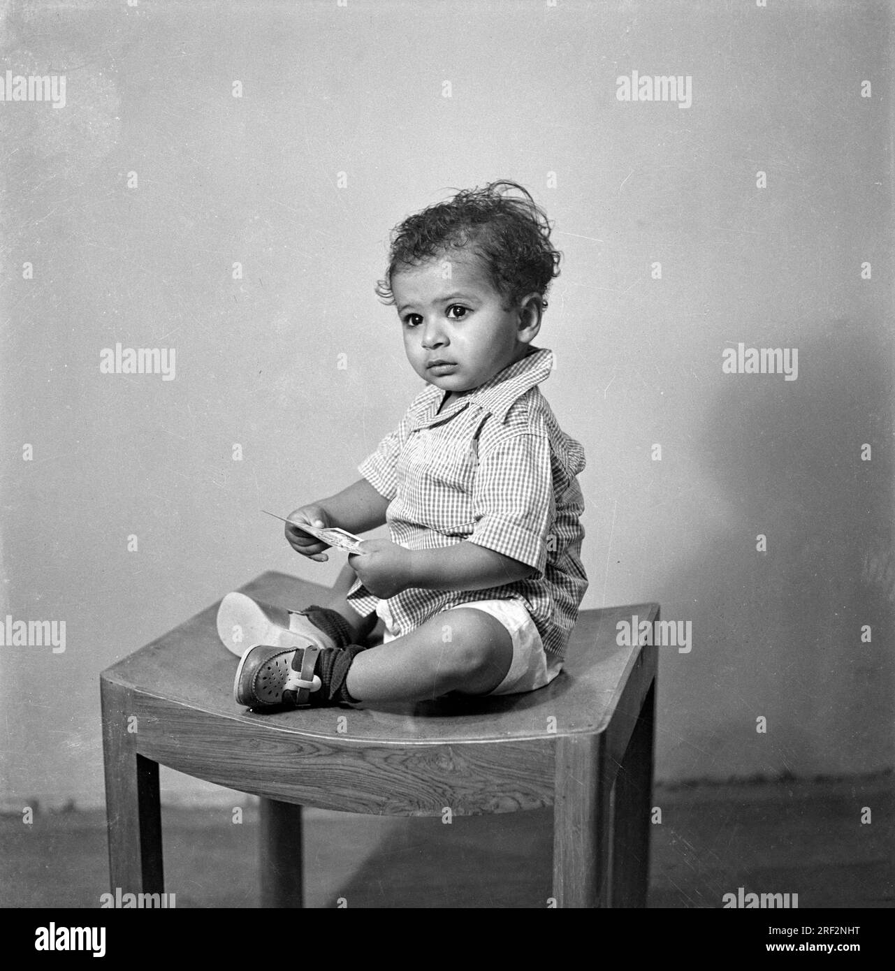 old vintage 1900s black and white studio portrait of Indian baby boy child sitting stool India 1940s Stock Photo