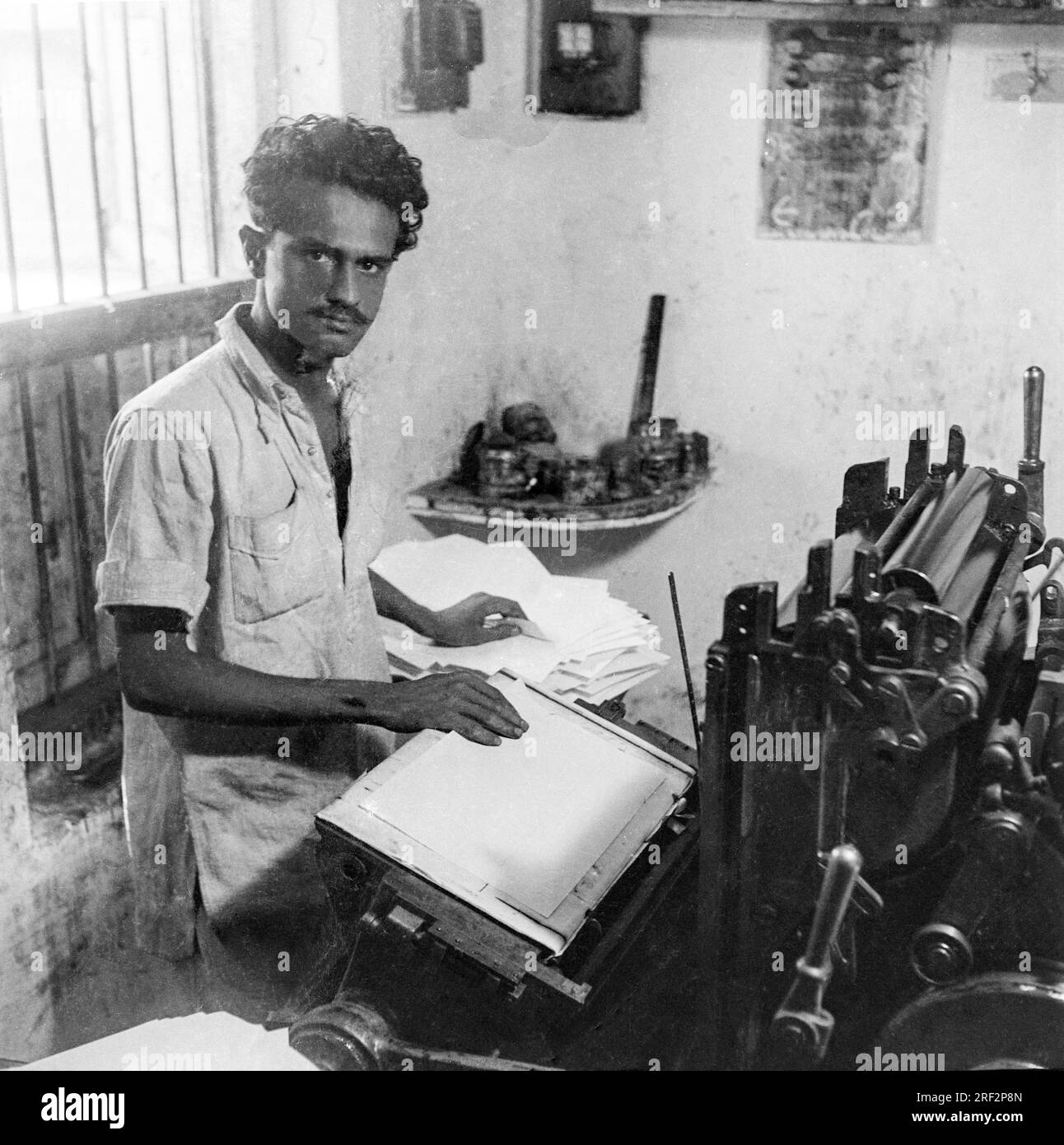 old vintage 1900s black and white picture of man working letter press printing machine India Stock Photo