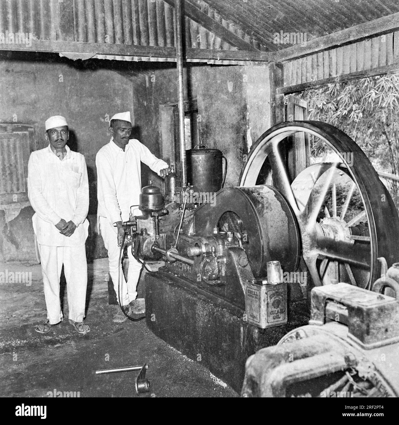 old vintage 1900s black and white picture of men working oil extraction machine Shell motor oil tin India Stock Photo