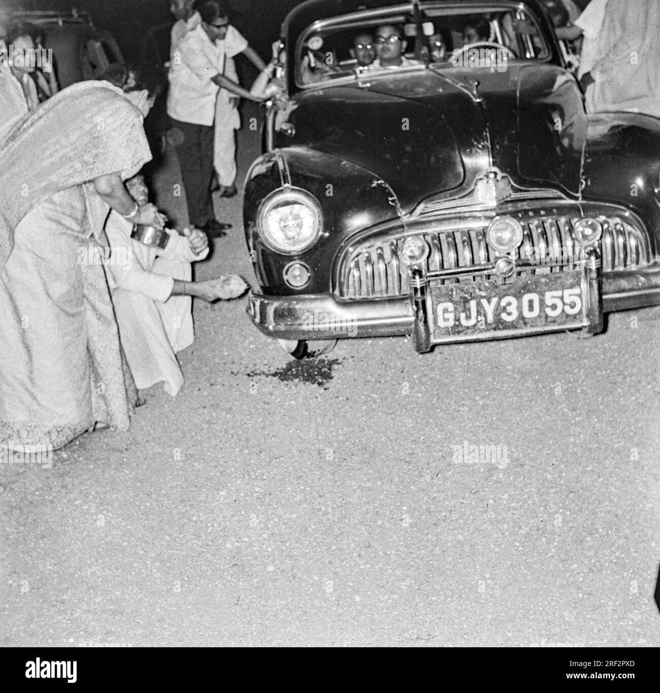old vintage 1900s black and white picture of breaking auspicious coconut welcome sign new Buick car GJY 3055 India 1940s Stock Photo