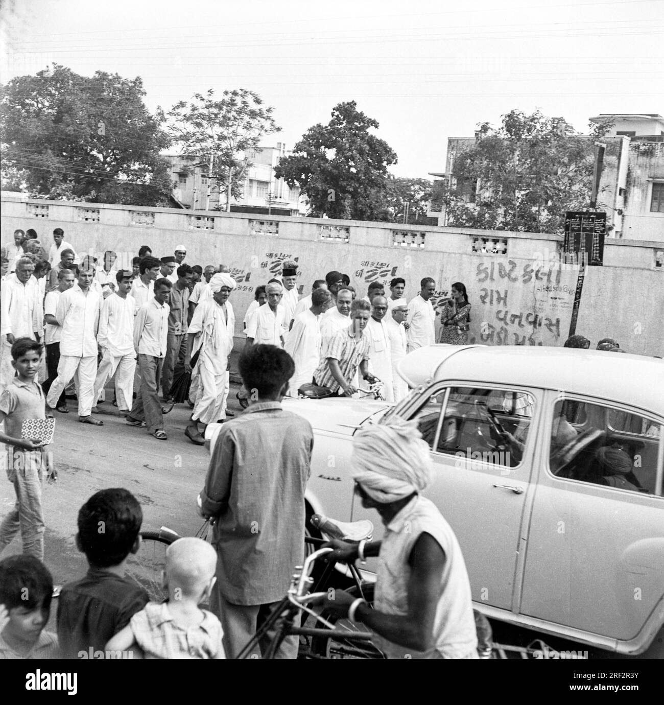 old vintage black and white 1900s picture of Indian street scene people procession Ambassador car  cycle bicycle India 1950s Stock Photo
