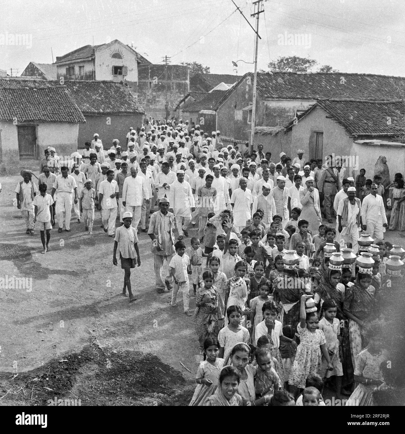old vintage 1900s black and white picture of village religious procession, women carrying pots, men wearing Gandhi cap, India Stock Photo