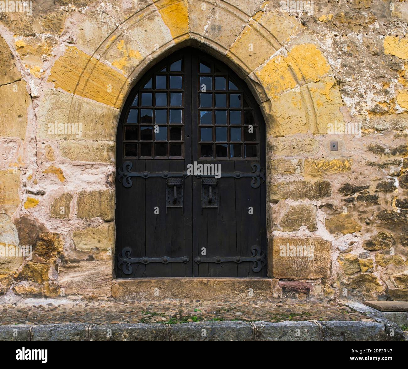 Ancient dark wooden door with pointed arch in stone wall, in the Cantabrian town of Santillana del Mar. Stock Photo