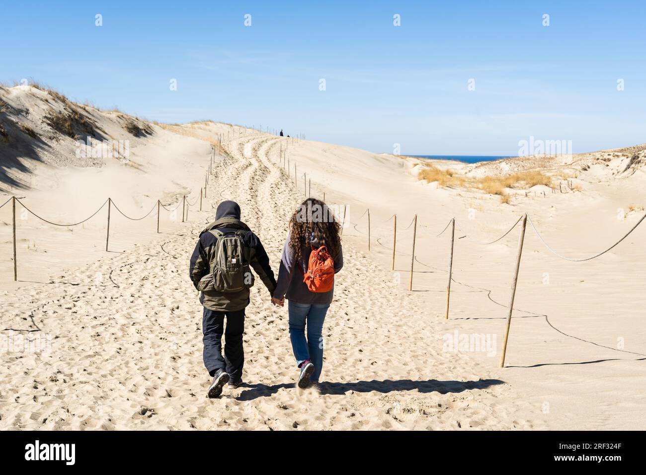 A couple of backpackers hand in hand walk along the hilly sand dunes on the Curonian Spit, Lithuania. Stock Photo