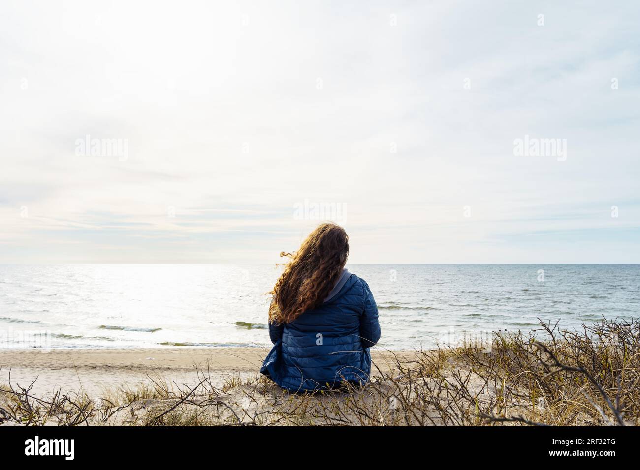 Long-haired curly plus size woman on the seashore, rear view. Stock Photo