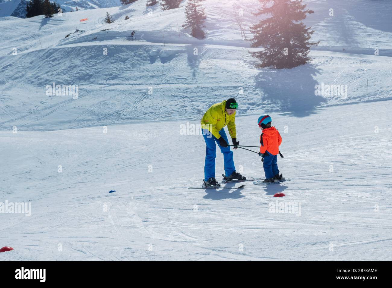 Dad glide backwards teaching little child to ski using poles Stock Photo