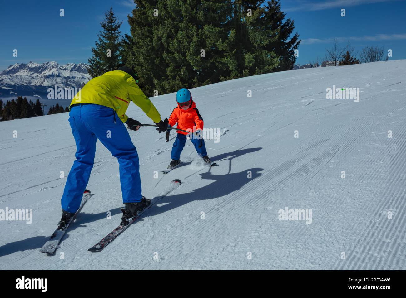 Dad teach little boy child to ski moving holding poles together Stock Photo