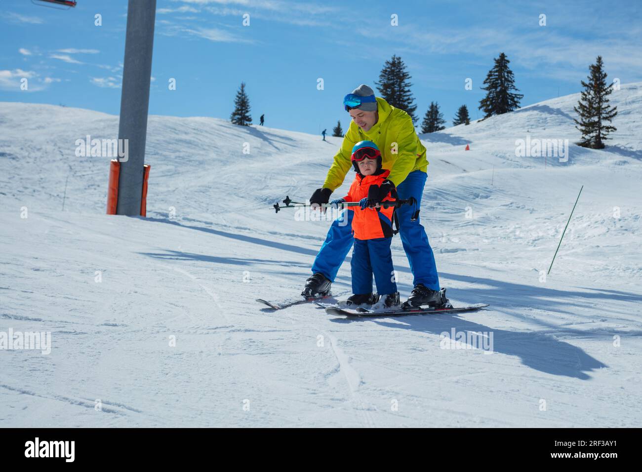 Adult teaches kid gliding behind holding ski poles together Stock Photo