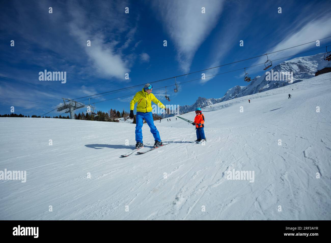 Father go downhill teach child to ski connected by poles Stock Photo