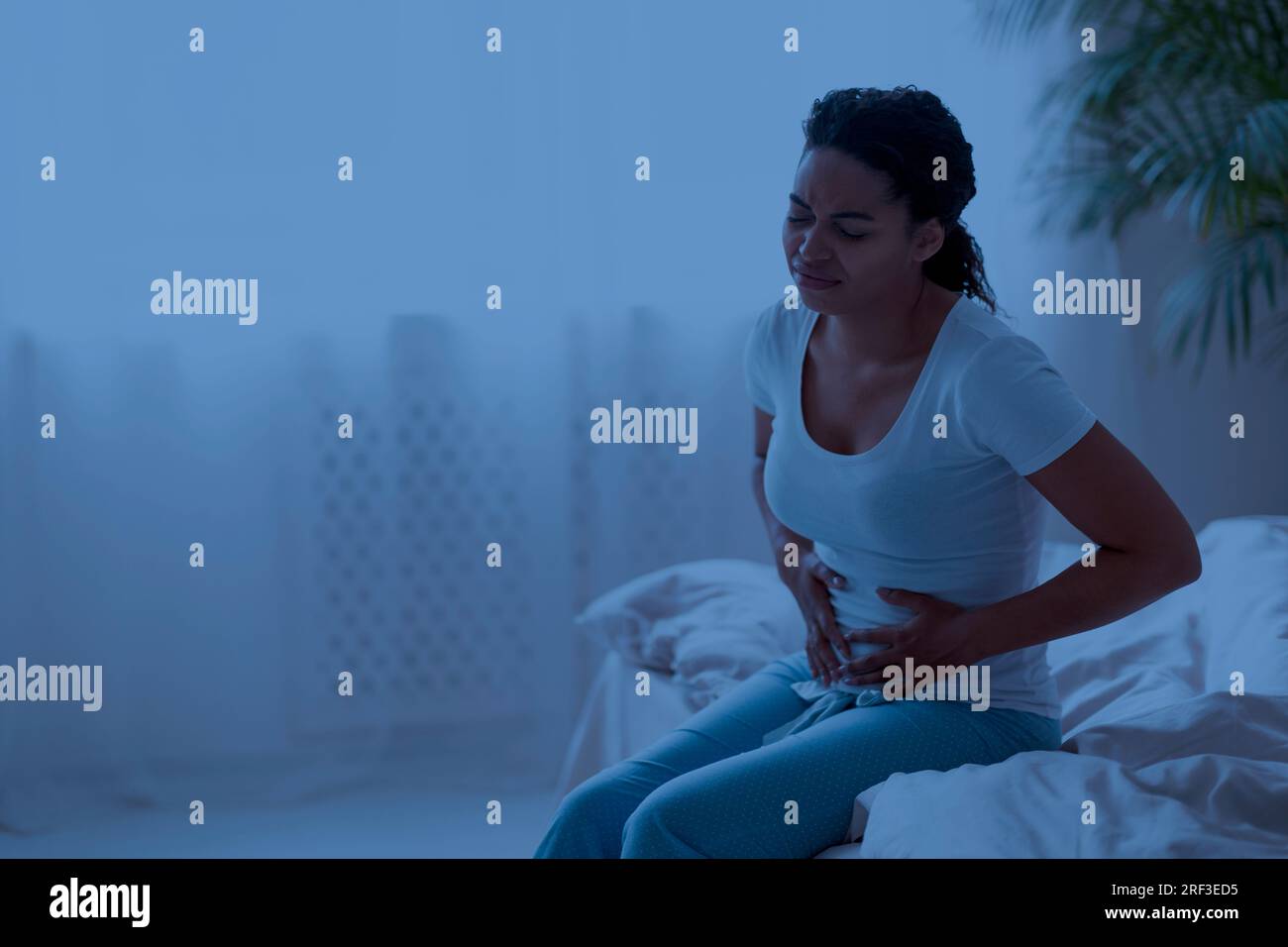 Unhappy young black woman suffering stomach pain in the night Stock