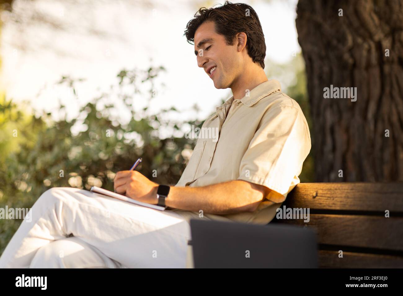 Millennial man student sitting on bench, doing homework Stock Photo