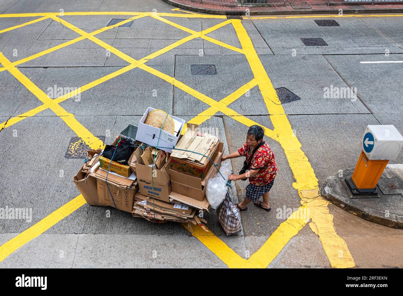 Old Chinese lady pushing cart through road junction while recycling