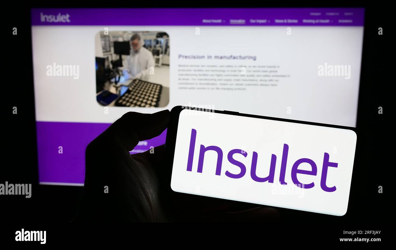 Person holding cellphone with logo of American medical device company Insulet Corporation on screen in front of webpage. Focus on phone display. Stock Photo