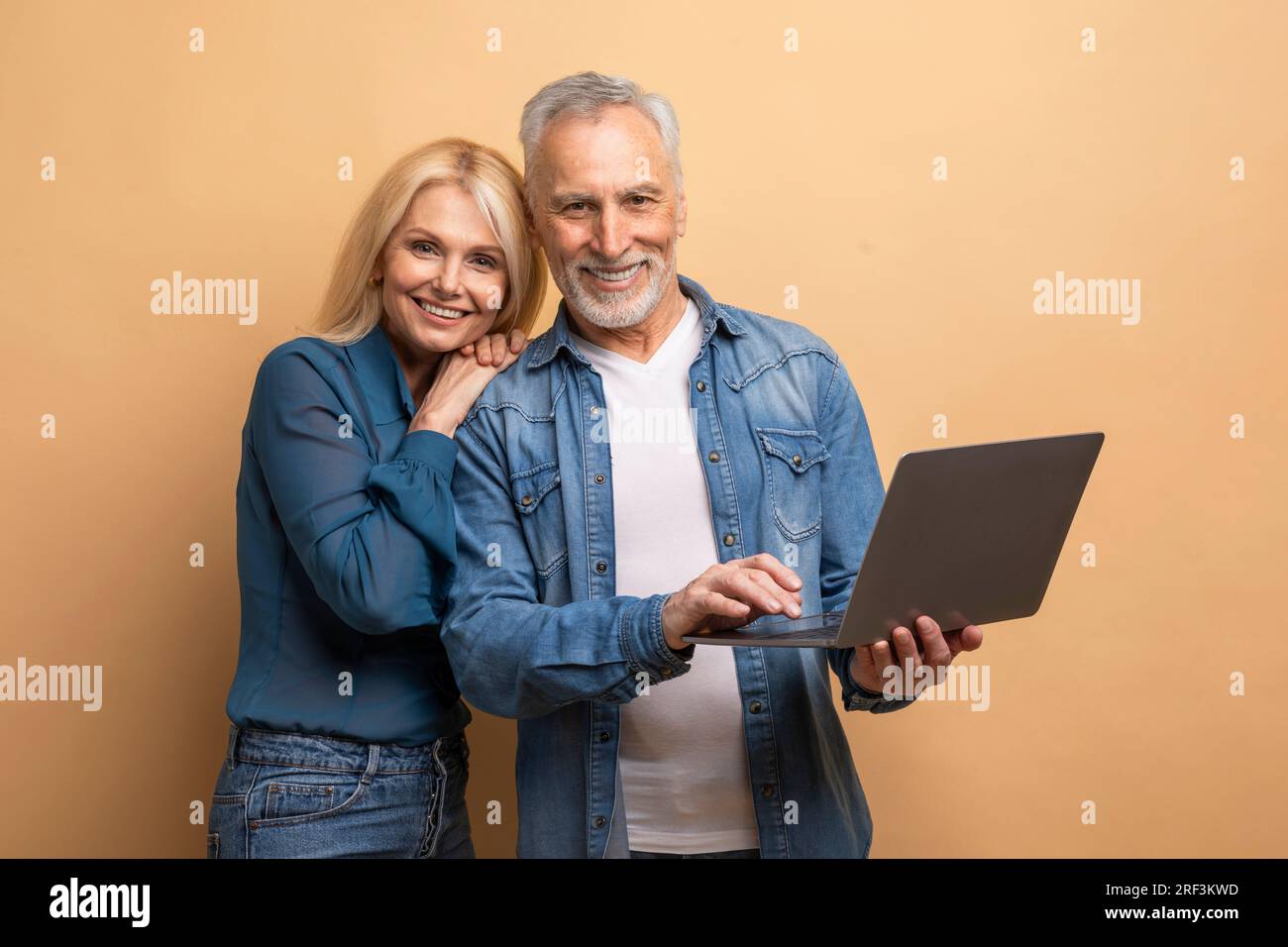 Loving elderly spouses using computer laptop on beige background Stock Photo