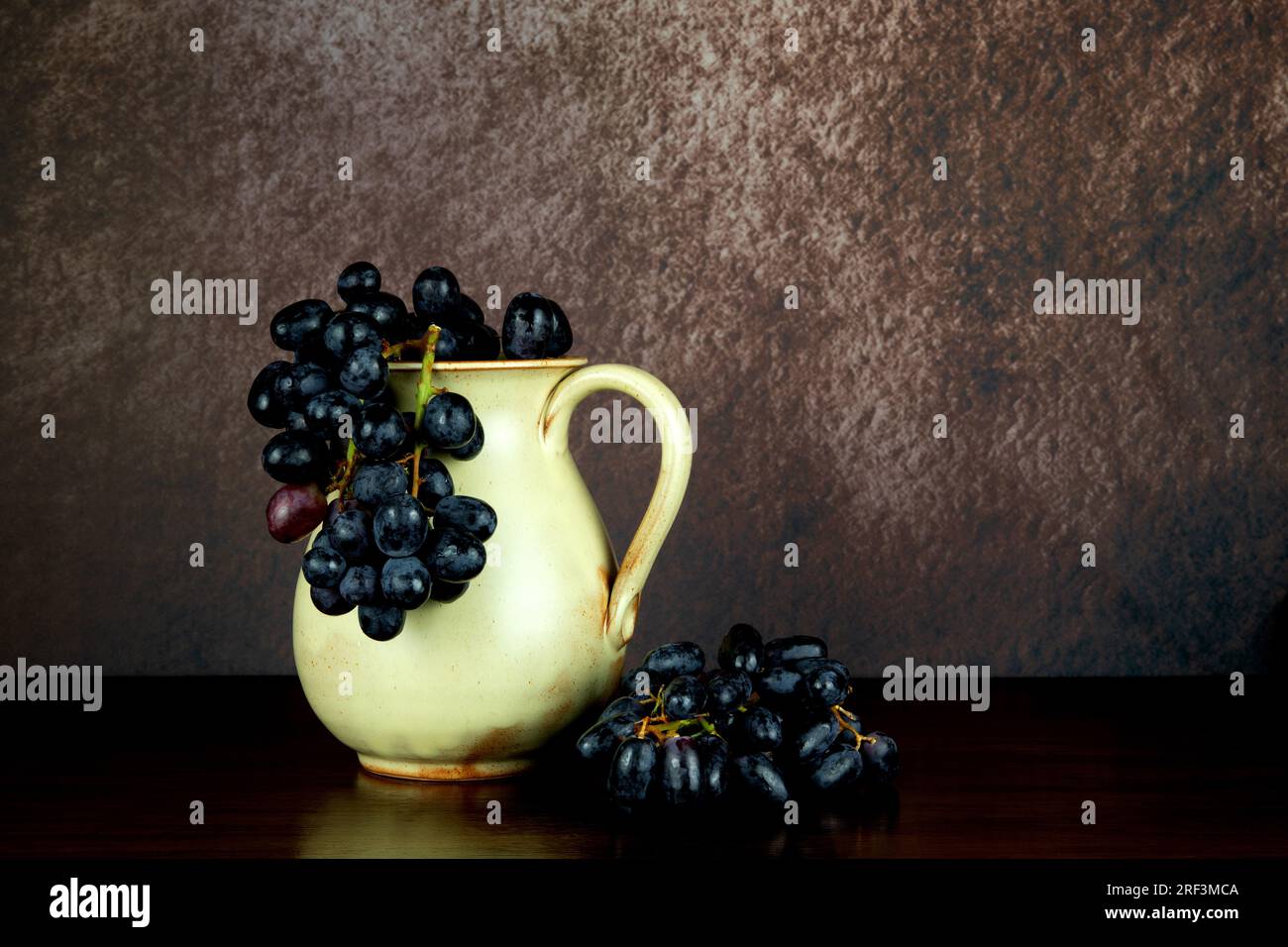 Old earthenware wine jug with bunches of grapes on a wooden table top Stock Photo