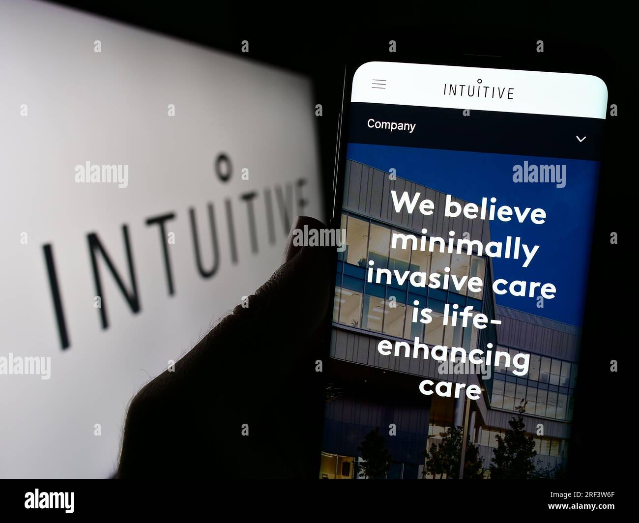 Person holding cellphone with webpage of US medical company Intuitive Surgical Inc. on screen in front of logo. Focus on center of phone display. Stock Photo