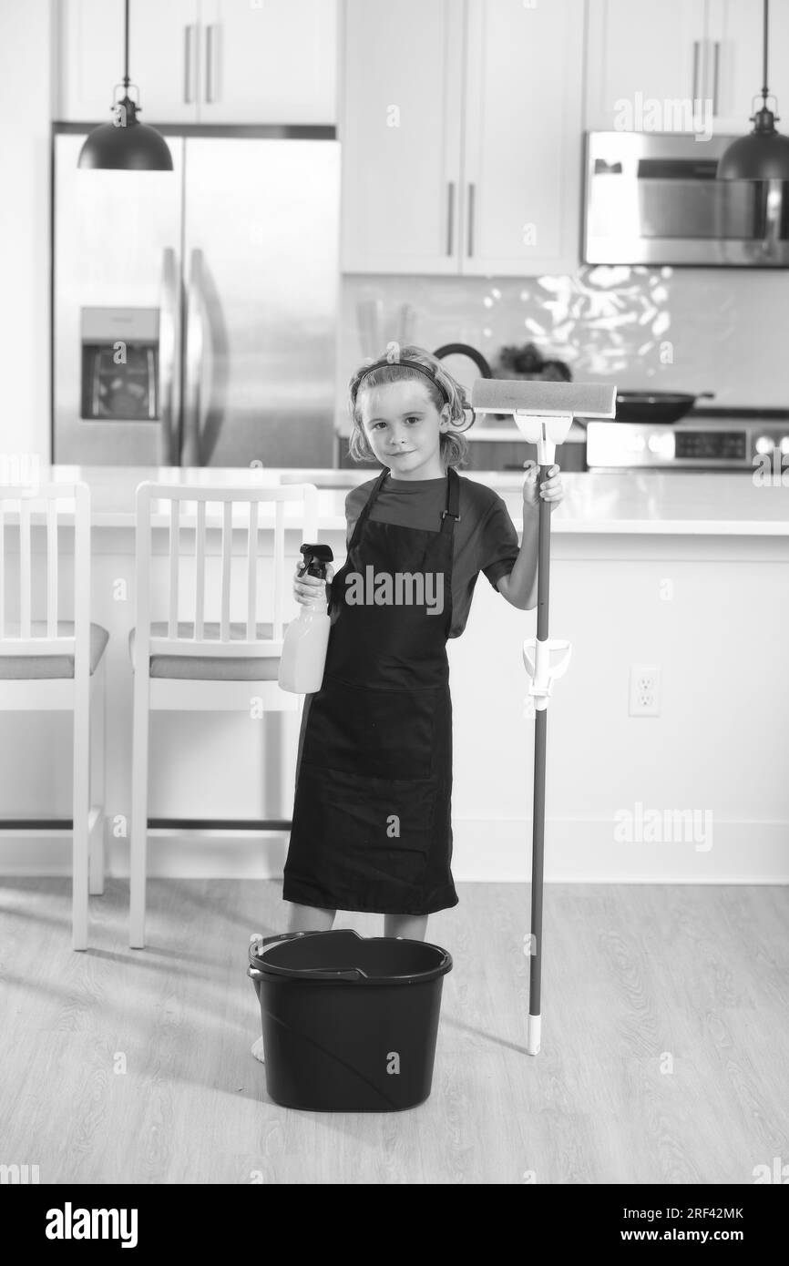 Child cleans at home concept. Kid cleaning with mop to help with housework. Little cute boy sweeping and cleaning, on kitchen background. Stock Photo