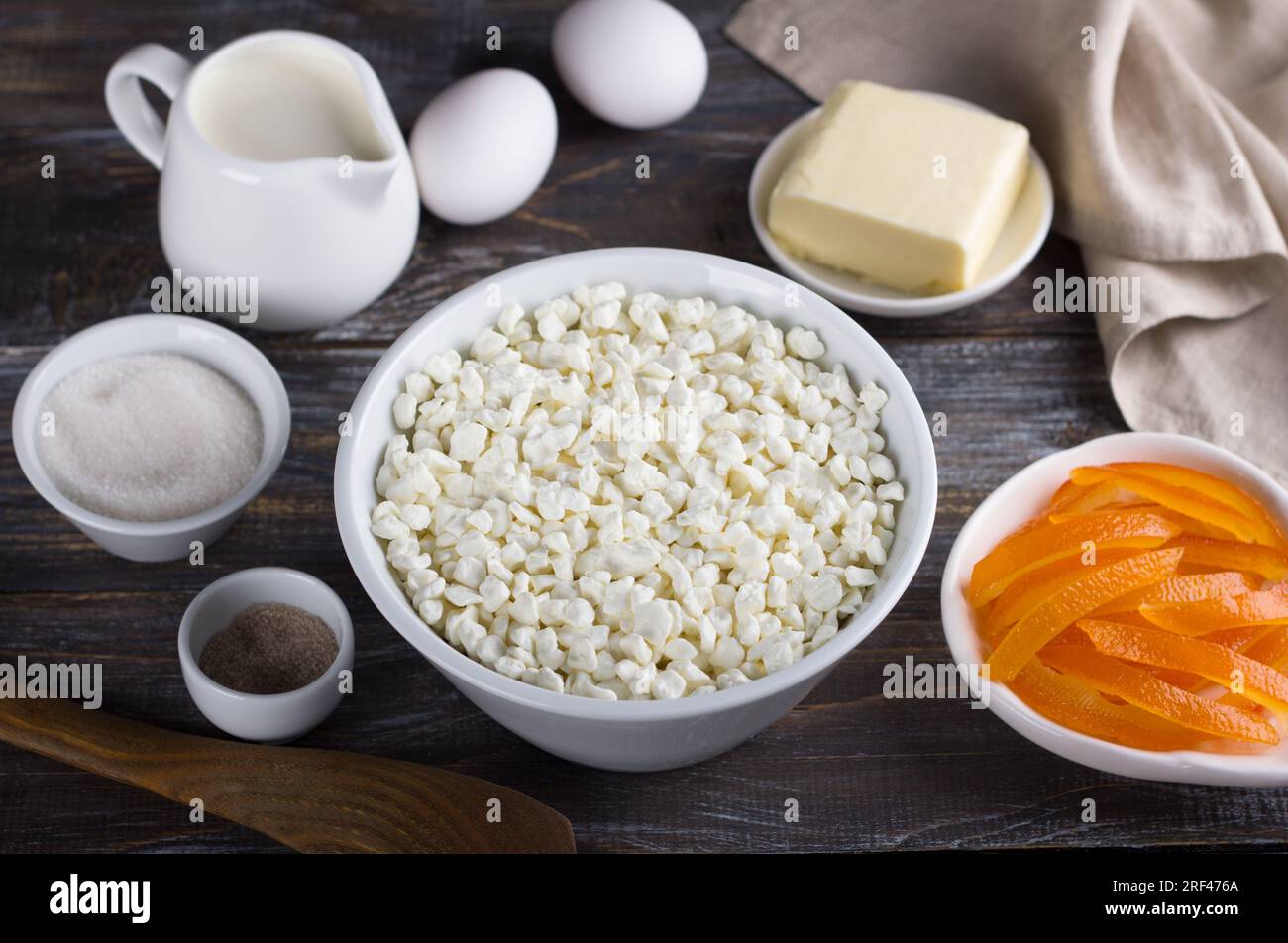Bowl with cottage cheese, candied oranges, cream, eggs, butter, sugar, vanilla sugar on a wooden background. Ingredients for home baking. Stock Photo