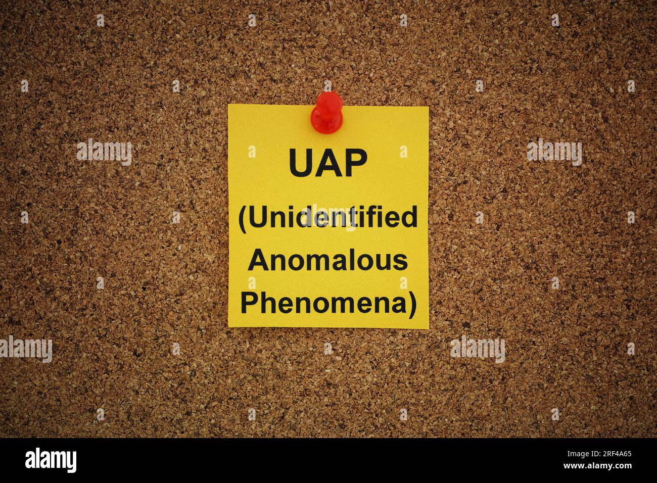 A yellow paper note with the words UAP (Unidentified Anomalous Phenomena) on it pinned to a cork board. Close up. Stock Photo