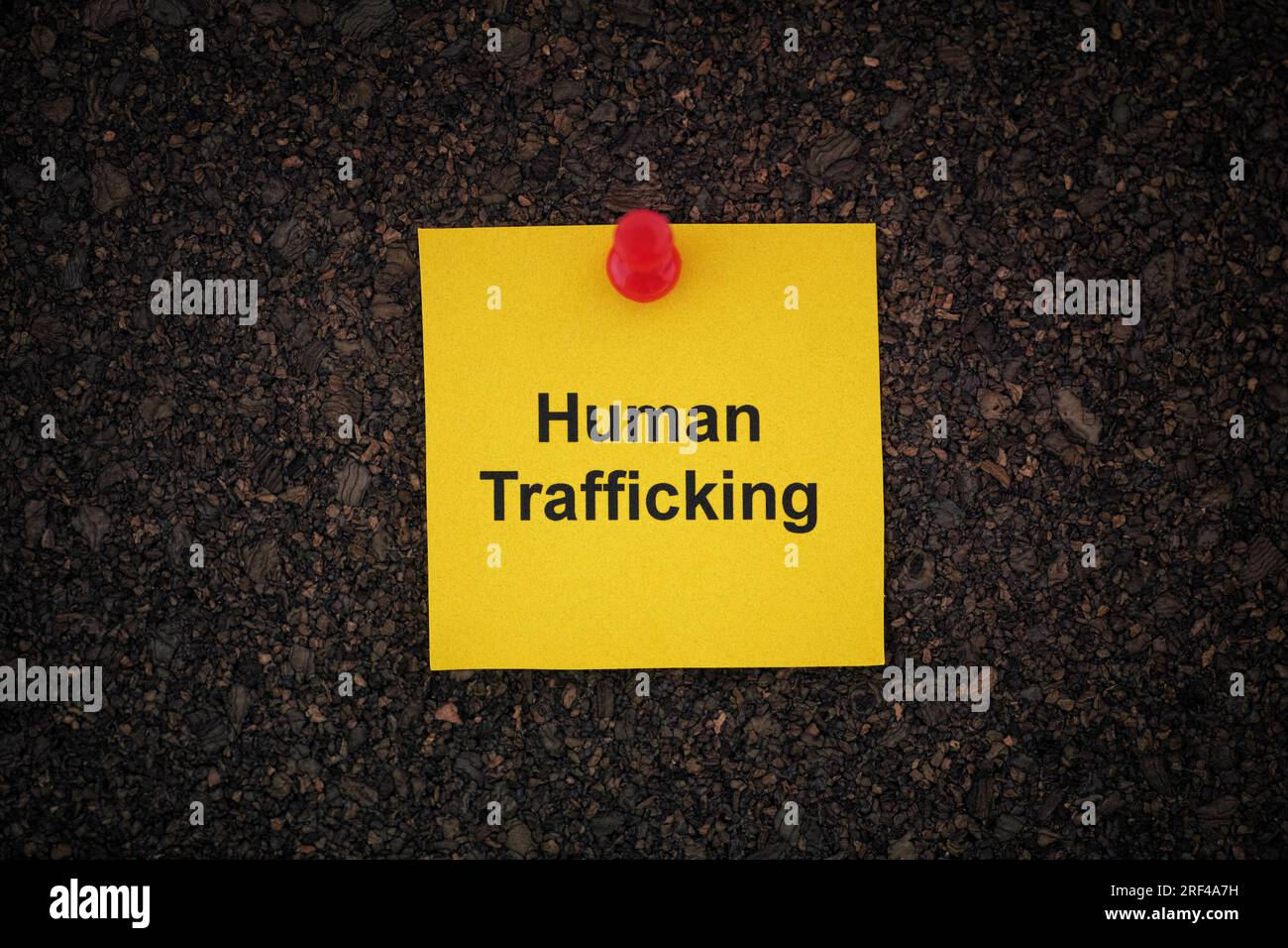 A yellow paper note with the words Human Trafficking on it pinned to a cork board. Close up. Stock Photo