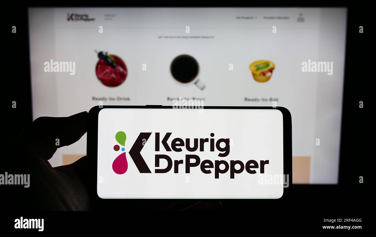 Person holding cellphone with logo of US beverage company Keurig Dr Pepper Inc. on screen in front of business webpage. Focus on phone display. Stock Photo