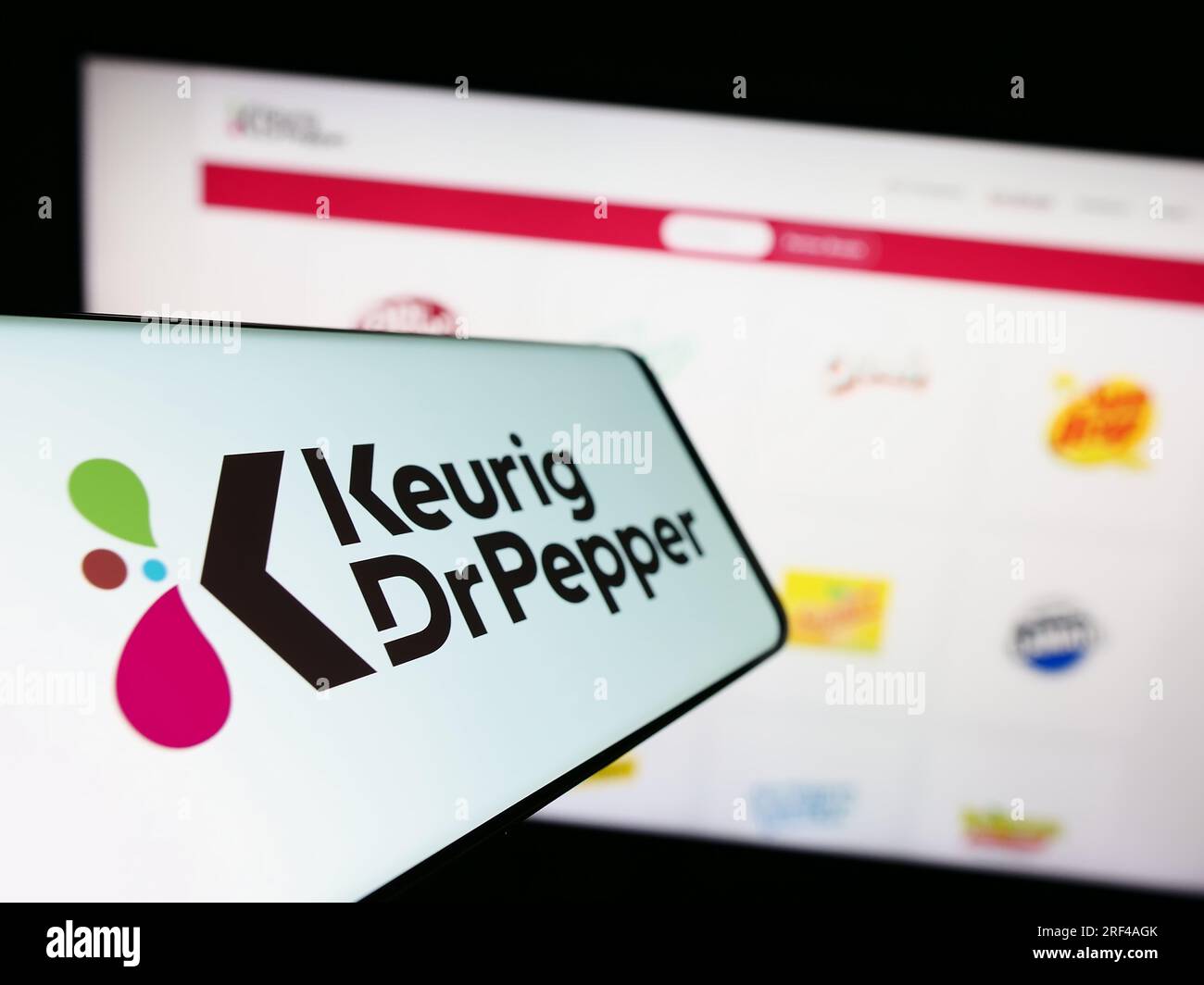 Smartphone with logo of American beverage company Keurig Dr Pepper Inc. on screen in front of website. Focus on center-left of phone display. Stock Photo