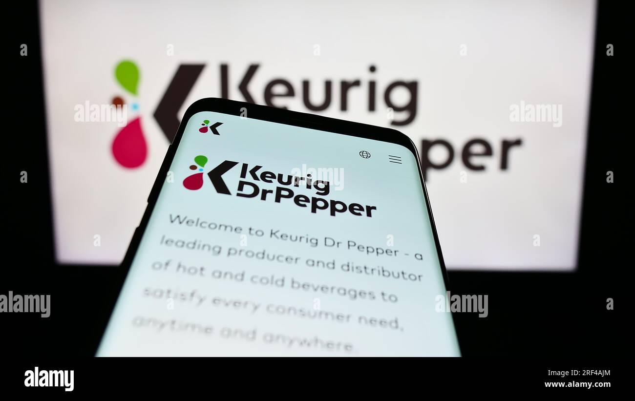 Mobile phone with webpage of US beverage company Keurig Dr Pepper Inc. on screen in front of business logo. Focus on top-left of phone display. Stock Photo