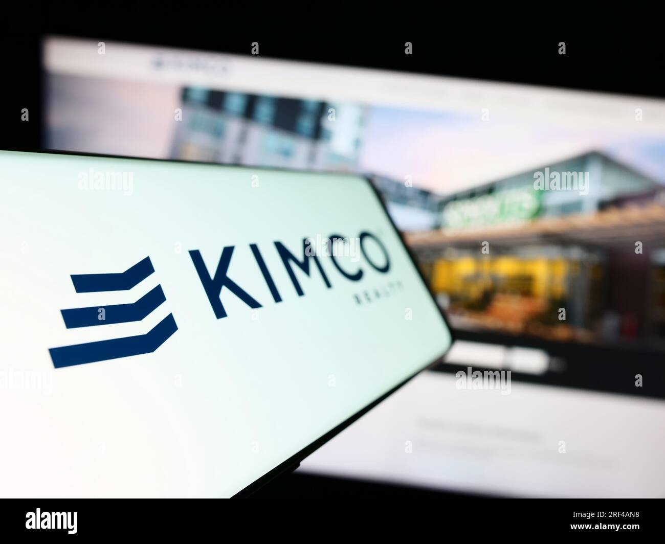 Cellphone with logo of American real estate company Kimco Realty Corporation on screen in front of website. Focus on left of phone display. Stock Photo