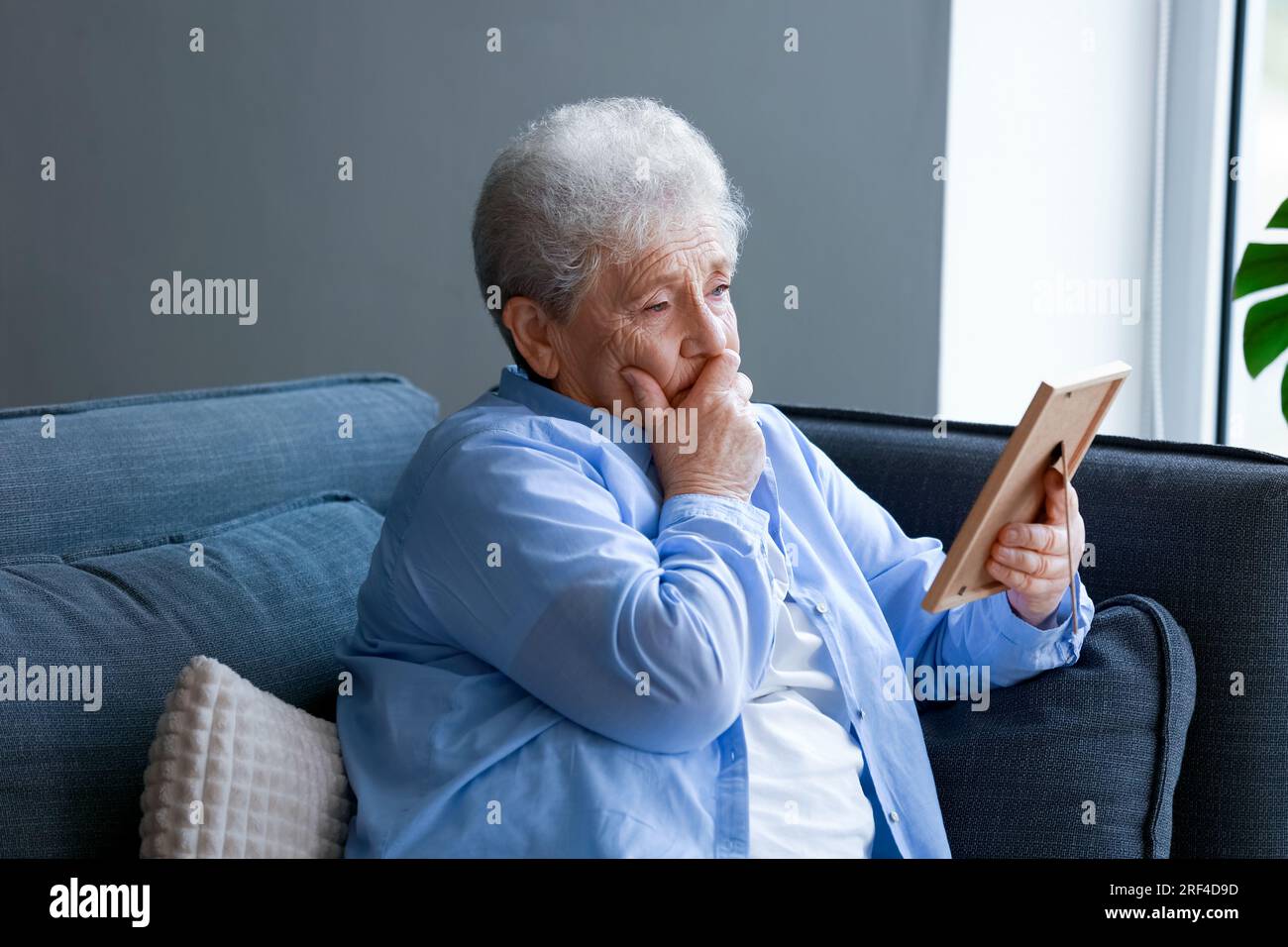 Sad senior woman with photo frame sitting on sofa at home Stock Photo