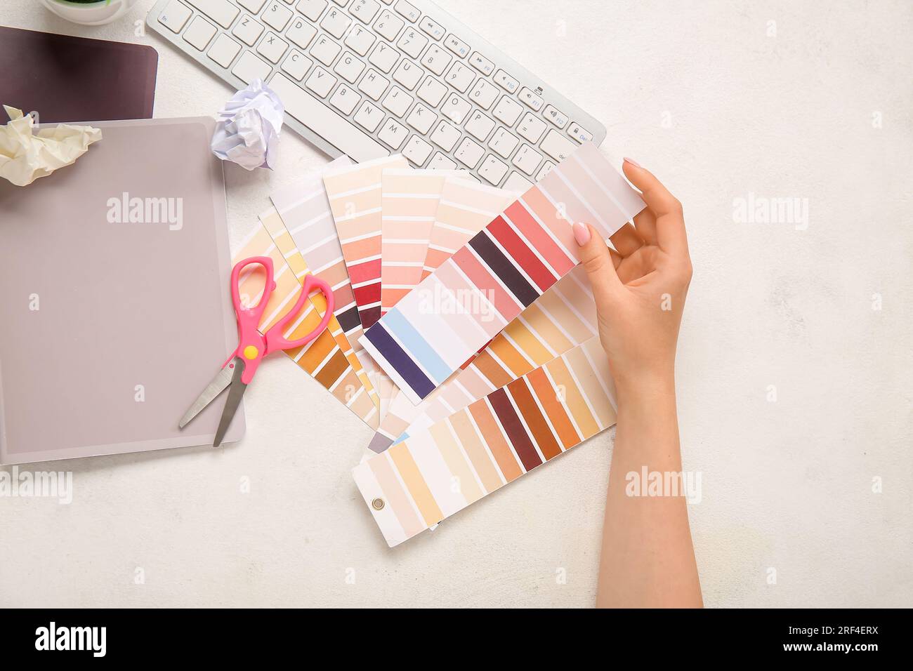 Female hand, color palettes, PC keyboard, notebooks and scissors on