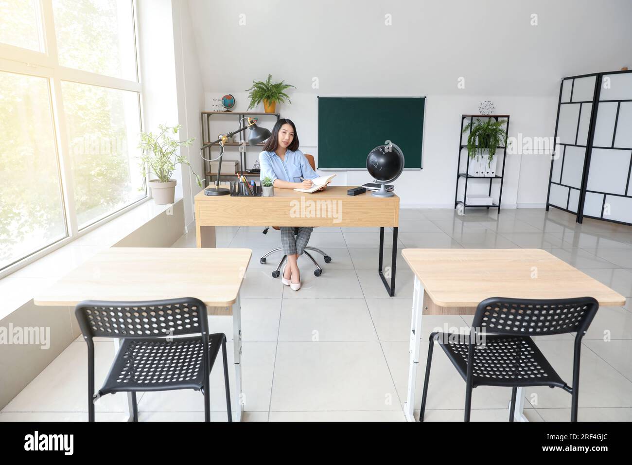 Female Asian teacher writing at table in classroom Stock Photo - Alamy