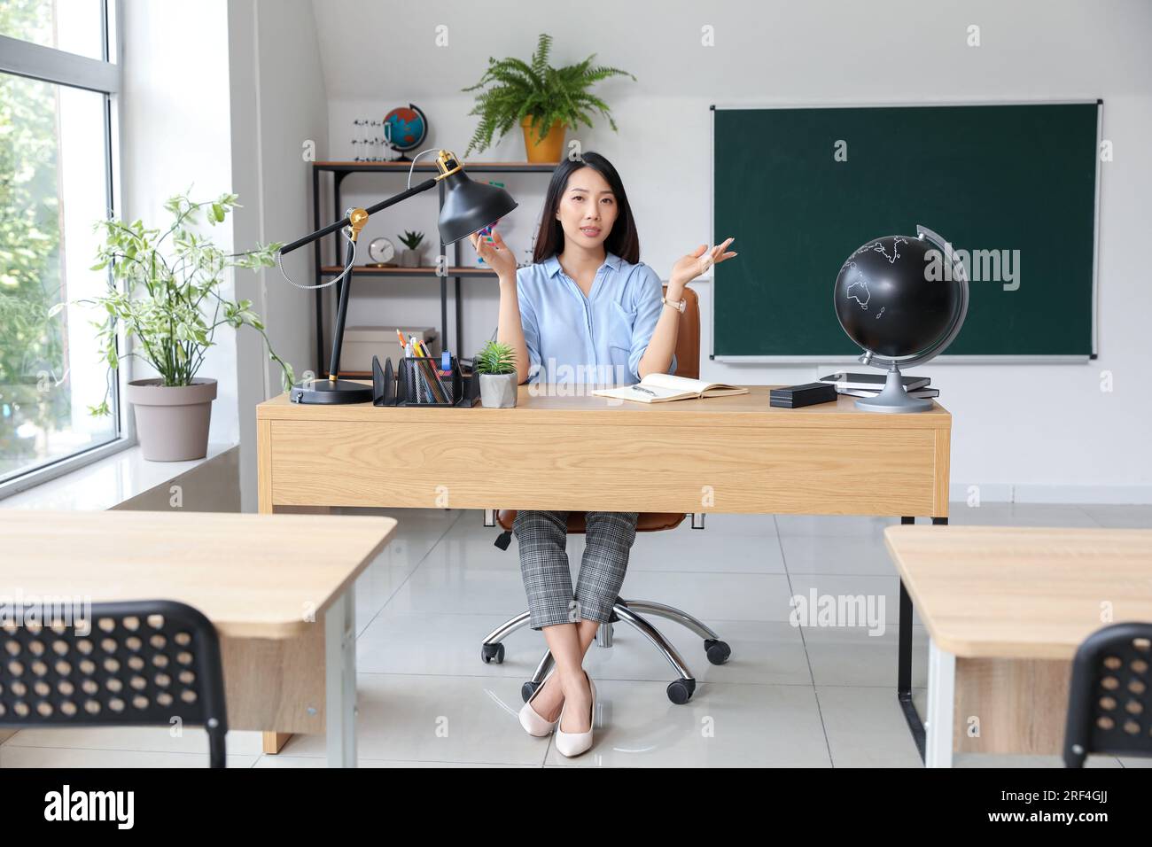 Female Asian teacher sitting at table in classroom Stock Photo - Alamy