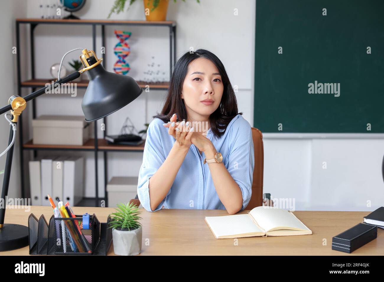Female Asian teacher sitting at table in classroom Stock Photo - Alamy