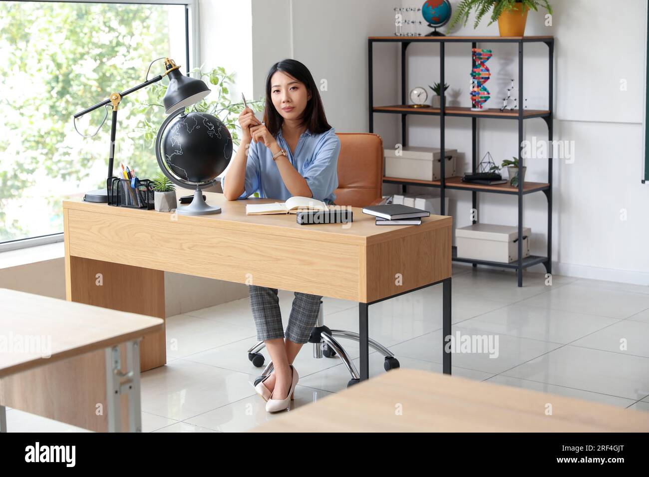 Female Asian teacher sitting at table in classroom Stock Photo - Alamy