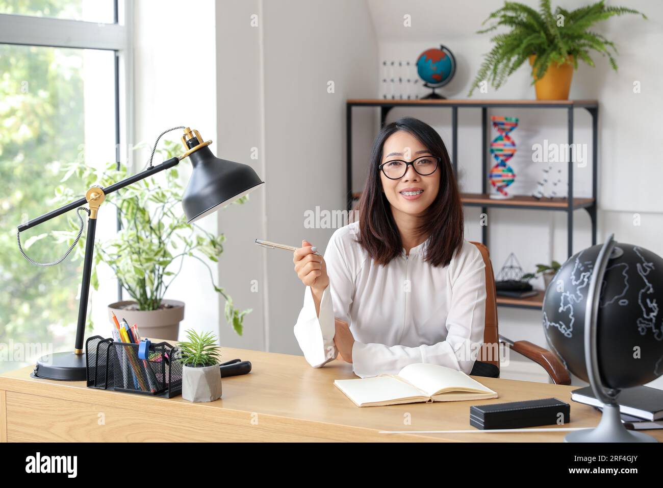 Female Asian teacher sitting at table in classroom Stock Photo - Alamy