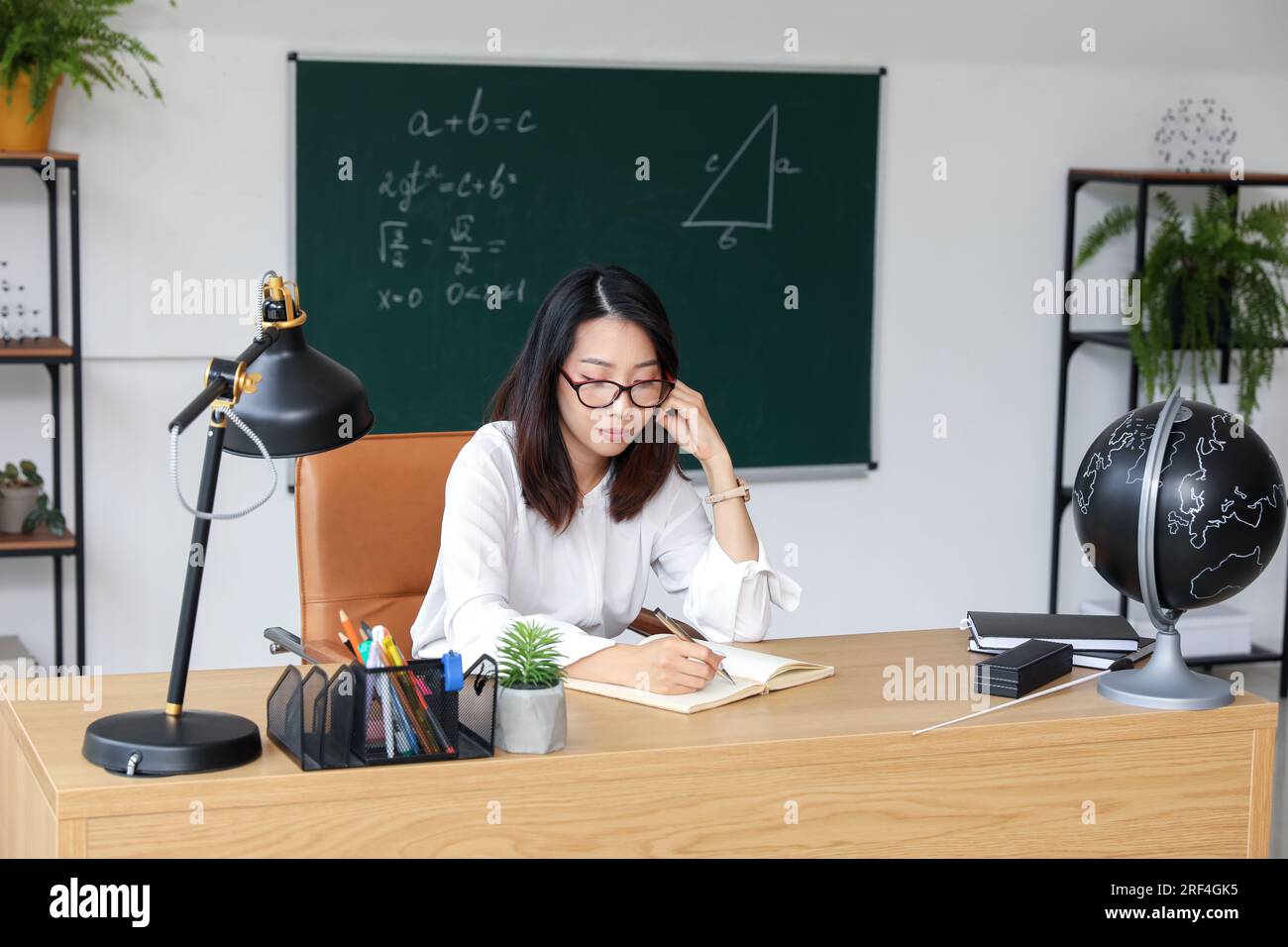 Female Asian teacher writing at table in classroom Stock Photo - Alamy