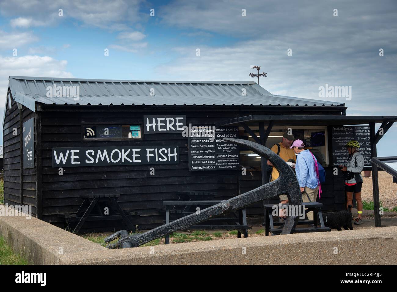 Customers buying from a traditional fish smokehouse on the pebble beach in the tourist seaside town of Aldeburgh on the Suffolk coast, England, UK Stock Photo