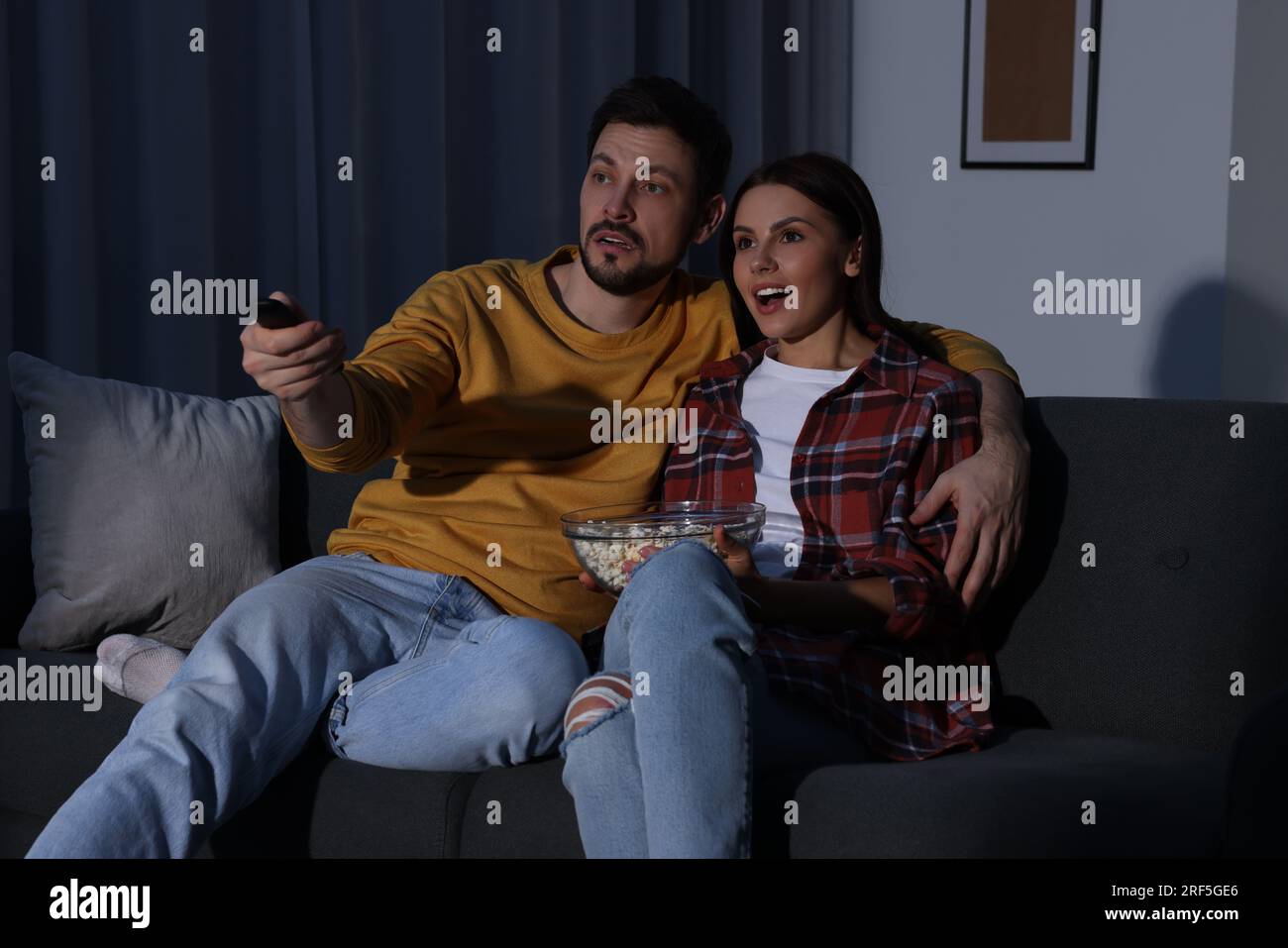 Couple watching TV at home in evening. Man changing channels with remote control Stock Photo