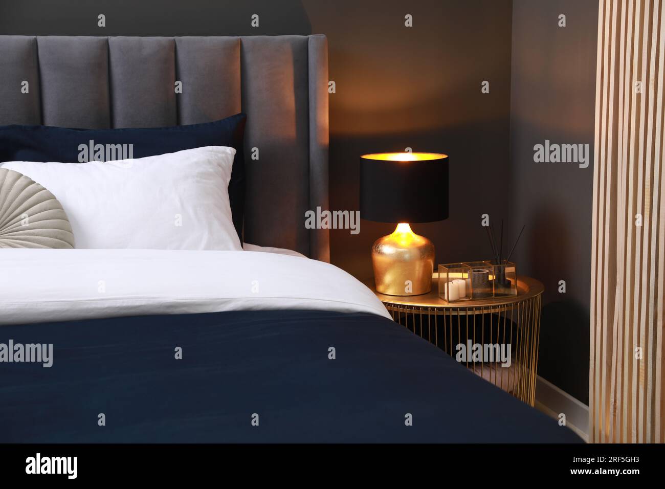 Comfortable bed with cushions, lamp and different decor on bedside table in room. Stylish interior Stock Photo