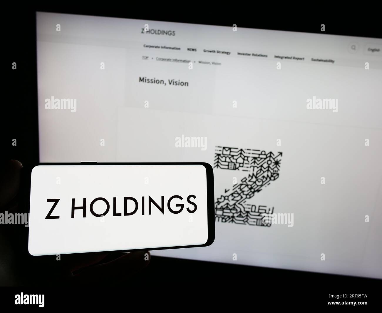 Person holding smartphone with logo of Japanese company Z Holdings Corporation on screen in front of website. Focus on phone display. Stock Photo