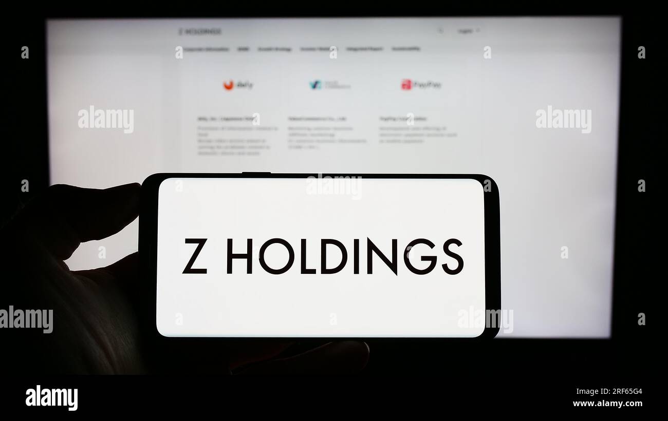 Person holding cellphone with logo of Japanese company Z Holdings Corporation on screen in front of business webpage. Focus on phone display. Stock Photo
