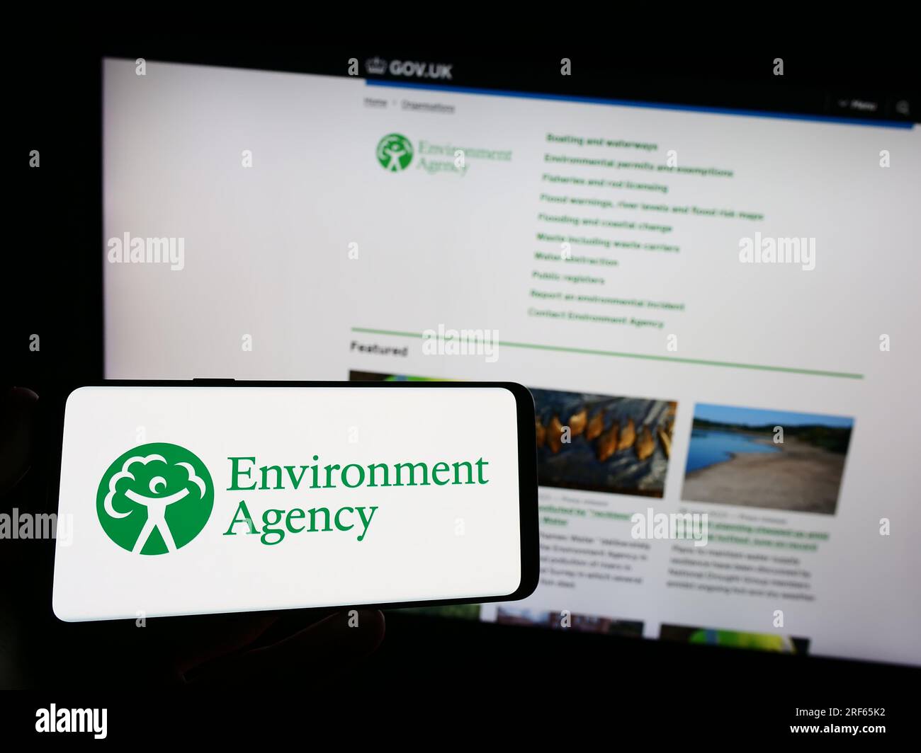 Person holding smartphone with logo of British public body Environment Agency (EA) on screen in front of website. Focus on phone display. Stock Photo