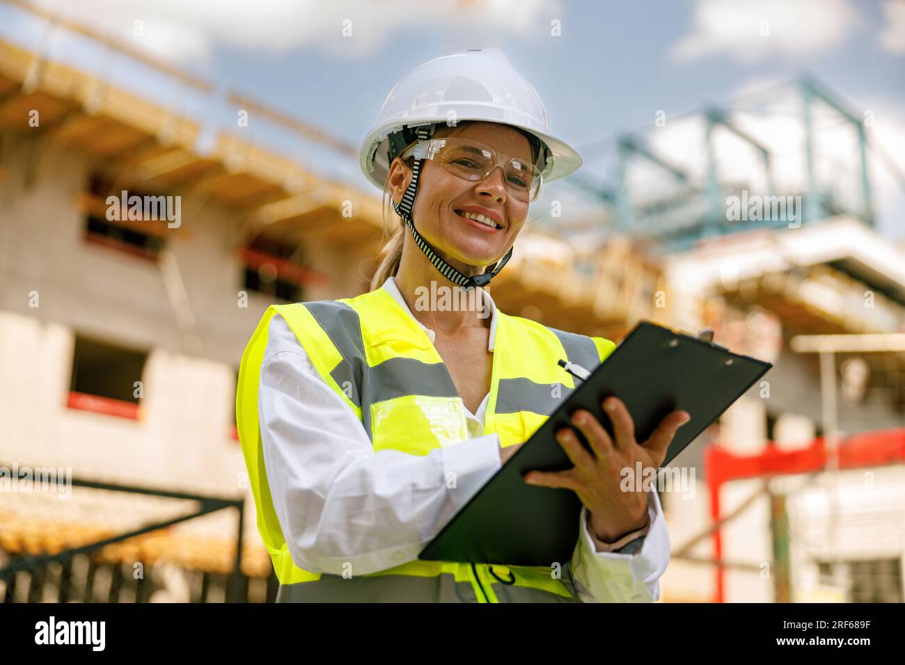 Professional female engineer in protective helmet making notes on construction site Stock Photo