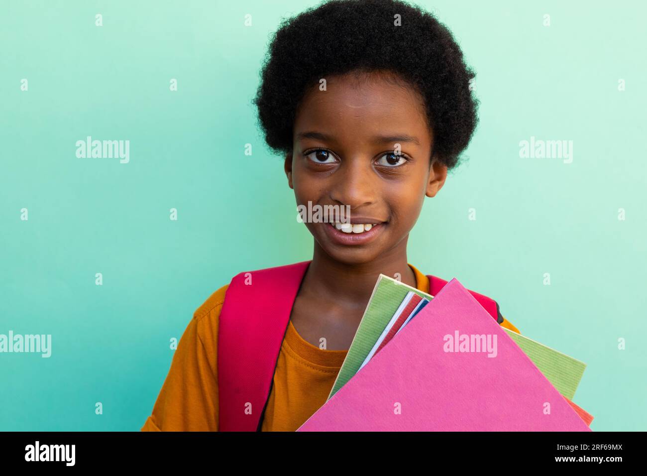 Portrait of happy biracial schoolboy with books wearing yellow tshirt over blue background Stock Photo