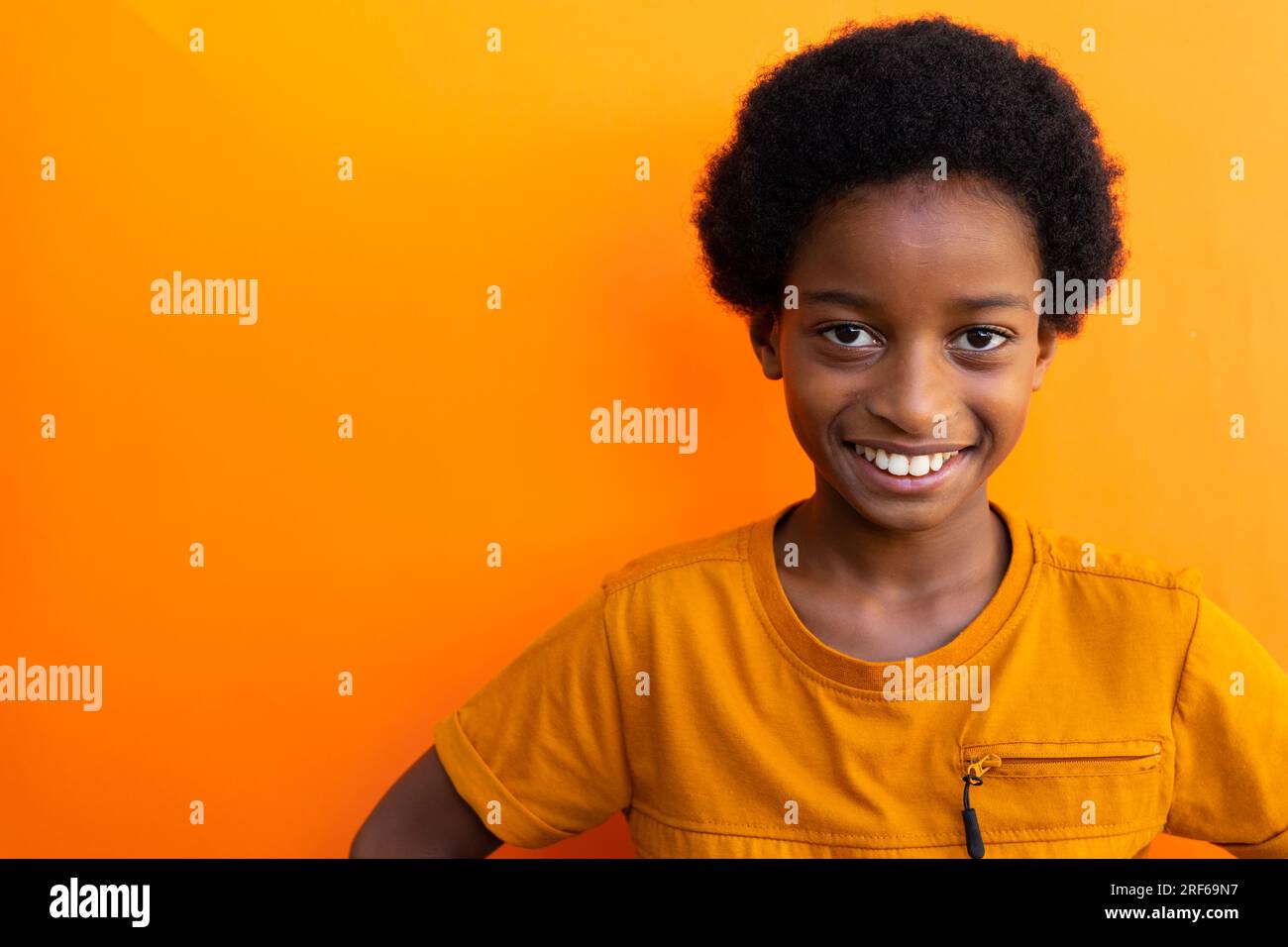 Portrait of happy biracial schoolboy wearing yellow tshirt over orange