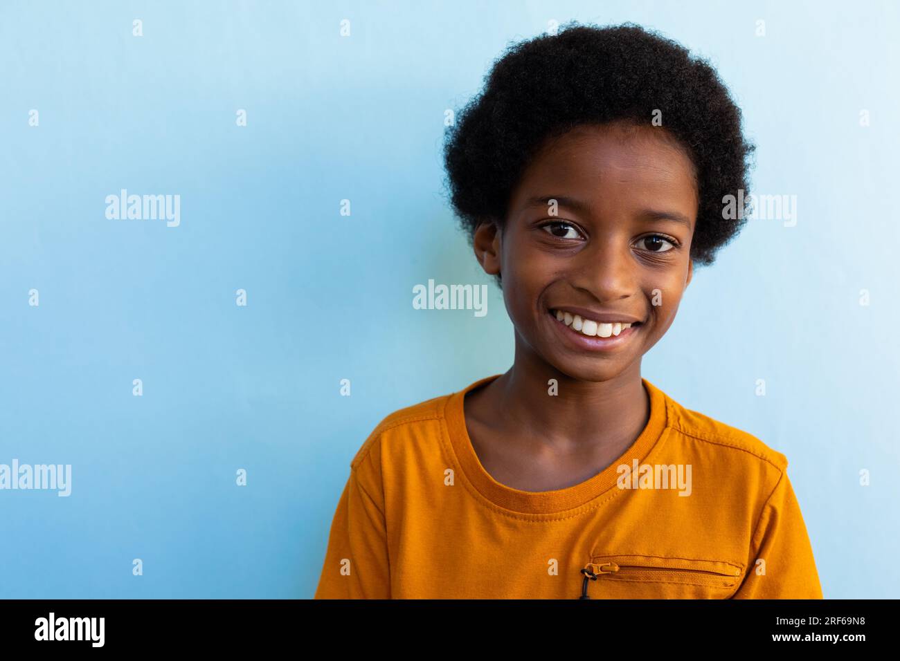 Portrait of happy biracial schoolboy wearing yellow tshirt over blue background, copy space Stock Photo
