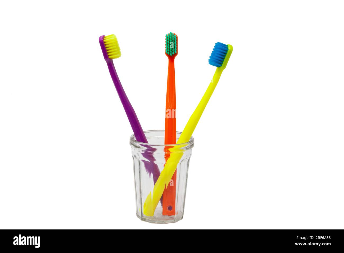 Three toothbrushes purple, orange and yellow with different colored bristles in a clear cup on
